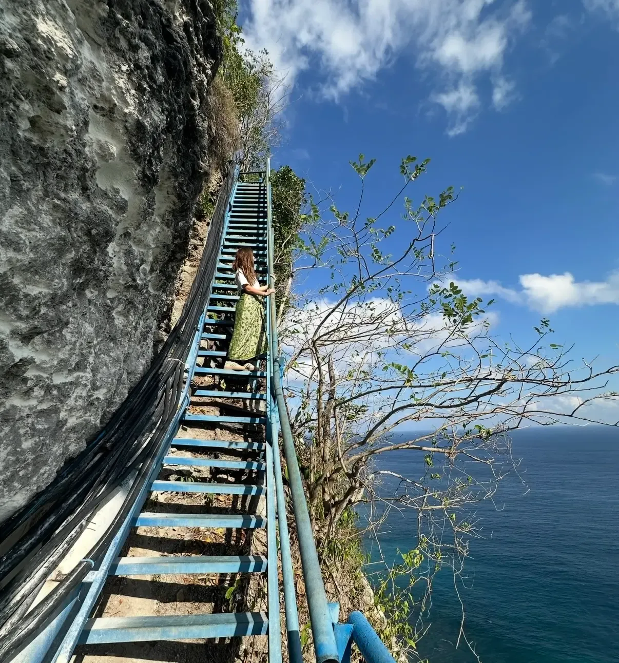 Blue stairs descending along the cliffside toward Peguyangan Waterfall in Nusa Penida
